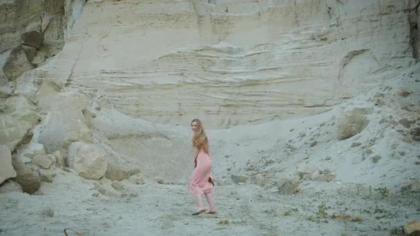 Όμορφο μοντέλο γυρίζει χαρούμενα κοντά στο λατομείο άμμου. Φαράγγι. Ξανθιά με ροζ φόρεμα και κίτρινο καπέλο. — Αρχείο Βίντεο