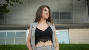 Kafkas görünümlü, gri takım elbiseli güzel bir kız modern ofislerin yanında yürüyor.