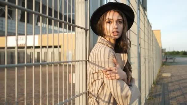 Belle fille modèle se tient et met un chapeau dans la rue. Brunette avec les cheveux longs dans un chapeau noir et manteau brun. Cadre de portrait de l'arrière — Video