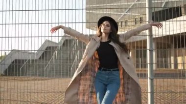 Güzel kız model sokakta durur ve bir şapka takar. Siyah şapkalı, kahverengi pelerinli, uzun saçlı esmer kadın. Arkadan portre çerçevesi