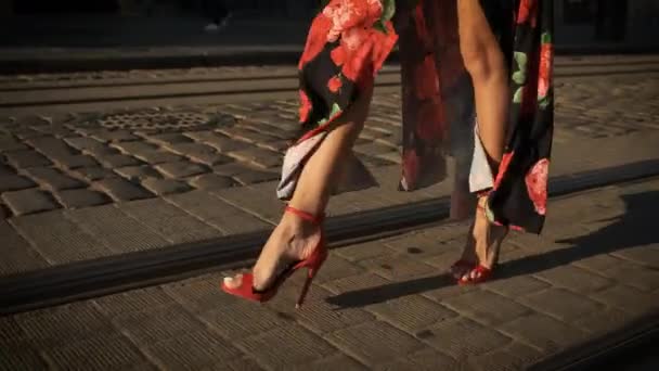 Hermosas piernas largas modelo caminando por la ciudad en tacones en zapatos rojos y un vestido largo — Vídeo de stock