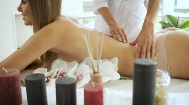 Modern spa merkezindeki güzel sarışın kıza çiçek ve mumlarla masaj masasında. Rehabilitasyon ve sağlık. Rahatla.