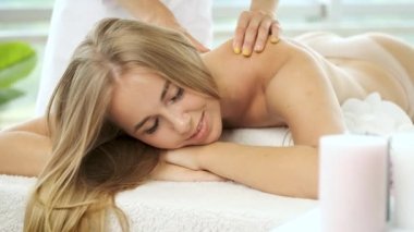 Modern spa merkezindeki güzel sarışın kıza çiçek ve mumlarla masaj masasında. Rehabilitasyon ve sağlık. Rahatla.