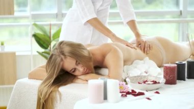 Modern spa merkezindeki güzel sarışın kıza çiçek ve mumlarla masaj masasında. Rehabilitasyon ve sağlık. Rahatla.