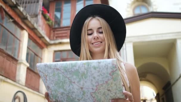 Γυναίκα τουρίστρια ξανθιά καυκάσια εμφάνιση περπατά γύρω από την πόλη πρωί σε ένα μακρύ φόρεμα και καπέλο κατέχει ένα χάρτη και εξερευνά την πόλη — Αρχείο Βίντεο