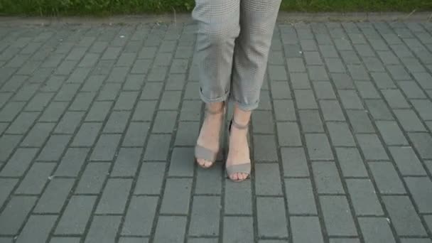 Длинные ноги на каблуках белой девушки в сером костюме, идущей рядом с современными офисами — стоковое видео