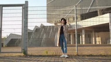 Güzel kız model sokakta durur ve bir şapka takar. Siyah şapkalı, kahverengi pelerinli, uzun saçlı esmer kadın. Arkadan portre çerçevesi