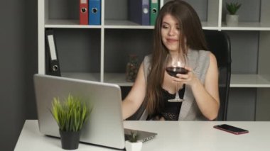 Genç, yakışıklı bir şirket yöneticisi ofiste oturmuş dizüstü bilgisayarla çalışıyor ve bir bardak kırmızı şarap içiyor. Depresyon. Rahatlama