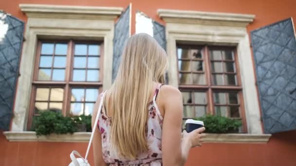 Femme touriste blonde apparence caucasienne se promène autour de la ville du matin dans une robe longue et chapeau tient une carte et explore la ville — Video