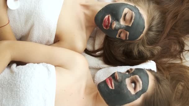 Девушки лежат в салоне на пилинг лица в современном спа-салоне. Омоложение кожи и здоровье. Модели позируют для камеры. Нанесение маски на лицо — стоковое видео
