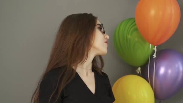 Ragazza caucasica che balla con borse regalo e palline colorate tra le mani su uno sfondo grigio della parete e sorride alla macchina fotografica — Video Stock