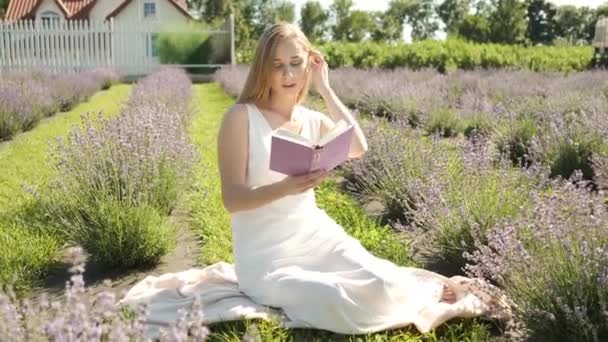 Vacker blond flicka 25 år gammal sitter i en lavendel fält läser en bok och avkopplande — Stockvideo