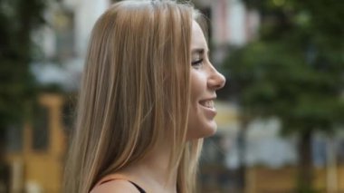 Sarışın sabah şehirde dolaşıyor ve kameraya gülümsüyor. Modellik. Yandan çerçeve