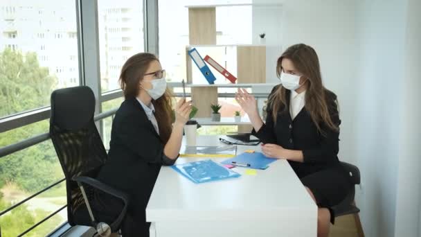 Mulheres de negócios sentam-se à mesa com máscaras durante uma pandemia em um escritório com janelas panorâmicas e negociam acordos de parceria. Boa sorte. — Vídeo de Stock