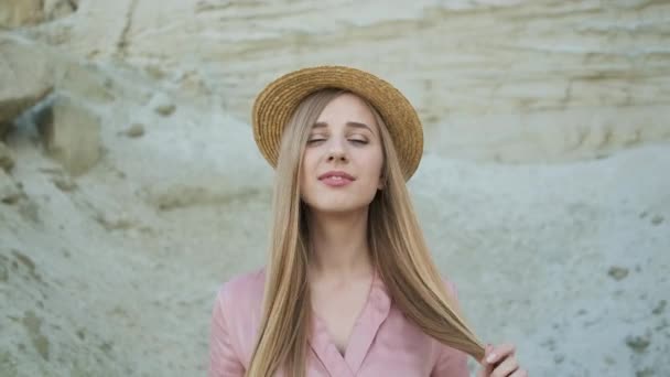 Krásná blondýnka model v růžových šatech a slaměný klobouk prochází kaňonem a pózuje pro kameru — Stock video