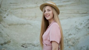 Pembe elbiseli ve hasır şapkalı güzel sarışın manken kanyonda yürür ve kameraya poz verir.