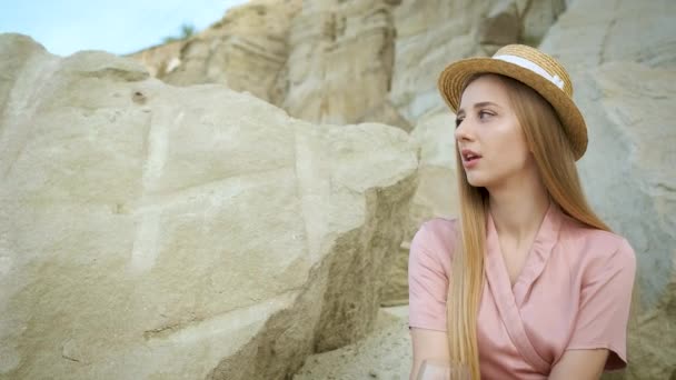 25 años chica turista en un sombrero rubio aspecto caucásico se sienta en una piedra en una cantera de arena y bebe una copa de vino tinto y se relaja. Disfrutando del cañón — Vídeos de Stock