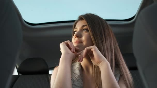 Belo sorriso de uma menina em um terno do diretor da companhia que se senta no carro com um telhado panorâmico. Motorista pessoal — Vídeo de Stock