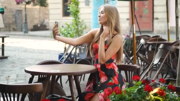 Blondynka kaukaska wygląd w pięknej sukience siedzi przy stole w historycznym miejscu rano i robi selfie przez telefon — Wideo stockowe