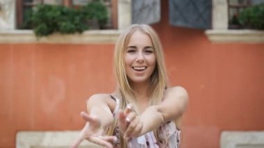 Elbise giymiş sarışın bir manken bir Avrupa şehrinde dolaşıyor ve kameraya poz veriyor. Güzel gülümseme