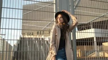 Güzel kız model sokakta durur ve bir şapka takar. Siyah şapkalı, kahverengi pelerinli, uzun saçlı esmer kadın. Arkadan portre çerçevesi