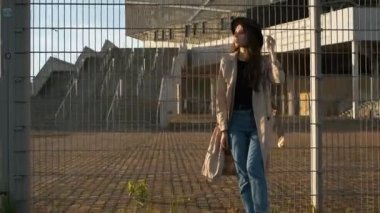 Güzel kız model sokakta durur ve bir şapka takar. Siyah şapkalı, kahverengi pelerinli, uzun saçlı esmer kadın. Arkadan portre çerçevesi