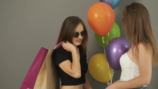 Καυκάσια κοπέλα χορεύει με τσάντες δώρων και χρωματιστές μπάλες στα χέρια της σε γκρι φόντο τοίχου και χαμογελά στην κάμερα — Αρχείο Βίντεο