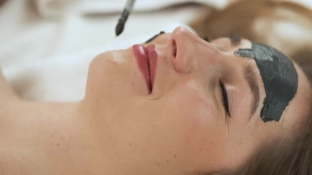 Mujer se encuentra sobre la mesa en un moderno spa y se relaja. Aplicar una máscara para rejuvenecer la piel. Salud y belleza — Vídeo de stock