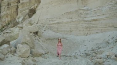 Güzel bir model bir kum ocağının yakınında dönüyor. Kanyon. Pembe elbiseli ve sarı şapkalı sarışın.