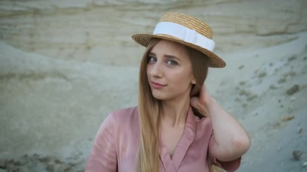 穿着粉色连衣裙头戴草帽的漂亮金发模特走过峡谷，摆出姿势面对镜头 — 图库视频影像