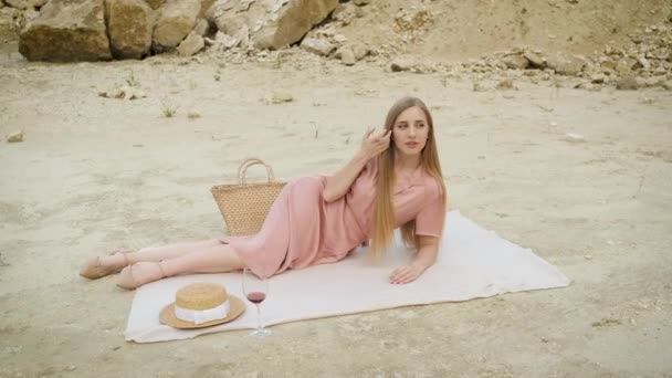 Blonde Frau auf einer Tischdecke in einem Sandsteinbruch mit einem Glas Rotwein liegend. Schlucht. Entspannen — Stockvideo