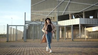 Genç ve güzel bir kız sokakta yürüyor. Siyah şapkalı, kahverengi pelerinli, uzun saçlı bir esmer. Arkadan portre çerçevesi