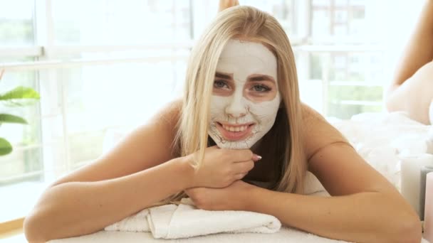 Linda modelo loira com uma máscara em seu rosto jaz na mesa no spa e posa para a câmera. Rejuvenescimento da pele — Vídeo de Stock