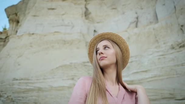 Turista giovane donna di aspetto caucasico bionda in un abito rosa con un cappuccio e una borsetta cammina attraverso il canyon e gode della bellezza della sabbia — Video Stock