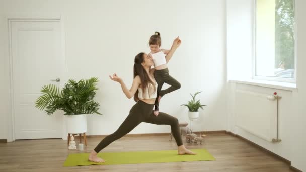 Mutter hält ihre Tochter auf dem Arm und praktiziert zu Hause Yoga. Meditation und Gesundheit. Entspannen — Stockvideo