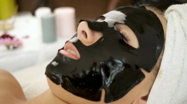 Yüzünde siyah bir maskeyle kaplıcada yatan bir kadın. Cilt tazeleme ve sağlık