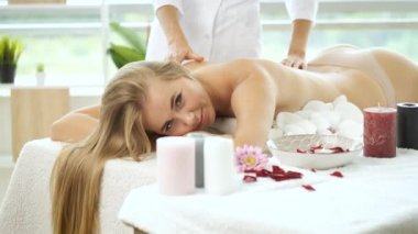 Modern spa merkezindeki güzel sarışın kıza çiçek ve mumlarla masaj masasında. Rehabilitasyon ve sağlık. Rahatla.