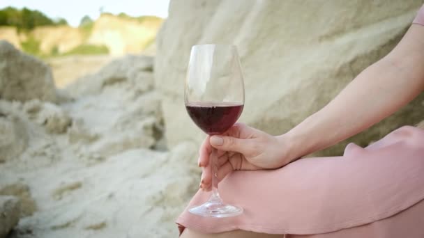 25-jährige Touristin mit blondem Hut und kaukasischem Aussehen sitzt auf einem Stein in einem Sandsteinbruch, trinkt ein Glas Rotwein und entspannt sich. Genießen Sie die Schlucht — Stockvideo