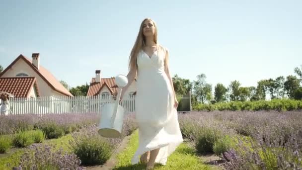 Flicka trädgårdsmästare tar hand om lavendel blommor häller vatten över dem. Lavendelodlingar — Stockvideo