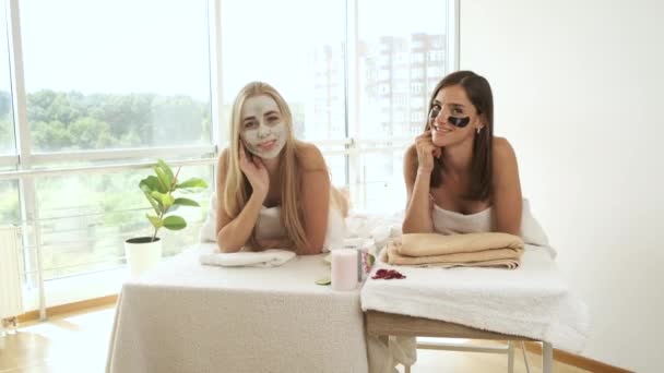 Dziewczyny leżą w salonie na peeling twarzy w nowoczesnym spa z panoramicznymi oknami. Odmładzanie skóry i zdrowie. Modelki pozujące do kamery. Nakładanie maski na twarz — Wideo stockowe