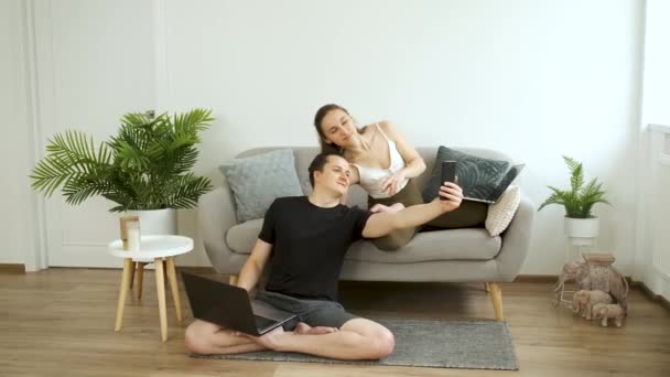 Mann und Frau sitzen allein auf der Couch, halten eine Flasche Wasser in der Hand und telefonieren per Videolink — Stockvideo