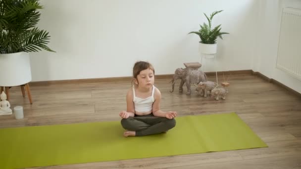 Petite fille blanche de 5 ans médite à la maison. Du yoga. Pose du lotus. Santé — Video