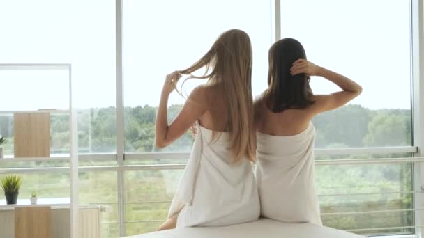 Niñas cubiertas con una toalla sentadas junto a la ventana panorámica en una habitación de un hotel de rascacielos con vistas a la ciudad — Vídeo de stock