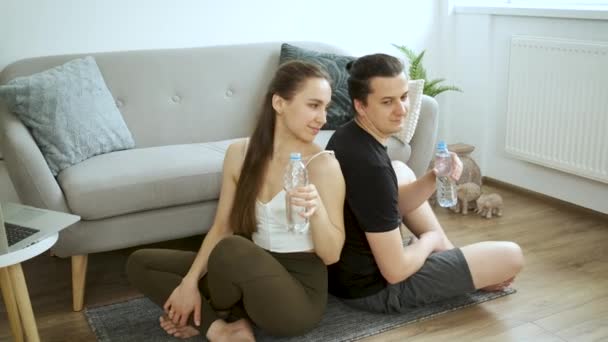 Homme et femme assis sur le sol à la maison près du canapé et de l'eau potable. Une famille heureuse. Santé et alimentation — Video