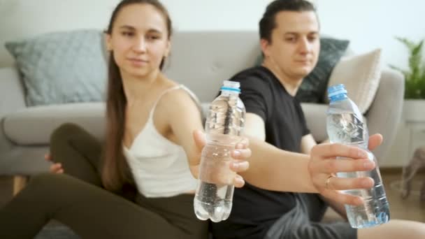 男人和女人坐在沙发旁边的地板上喝水。一个幸福的家庭健康和饮食 — 图库视频影像