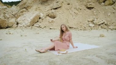 Sarışın kadın elinde bir bardak kırmızı şarapla bir kum ocağında masa örtüsünün üzerinde yatıyor. Kanyon. Rahatla.