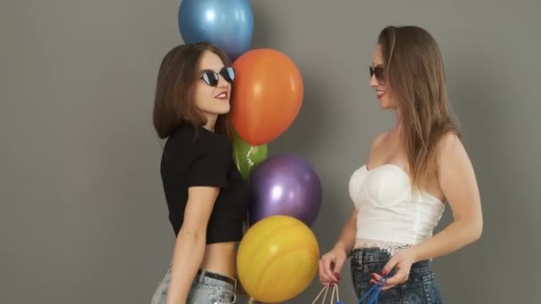 Καυκάσια κοπέλα χορεύει με τσάντες δώρων και χρωματιστές μπάλες στα χέρια της σε γκρι φόντο τοίχου και χαμογελά στην κάμερα — Αρχείο Βίντεο