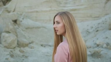 Pembe elbiseli ve hasır şapkalı güzel sarışın manken kanyonda yürür ve kameraya poz verir.