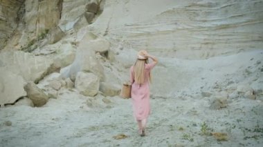 Kafkas görünümlü, pembe elbiseli, kapüşonlu ve çantalı genç bir kadın kanyonda yürüyor ve kumların güzelliğinin tadını çıkarıyor.