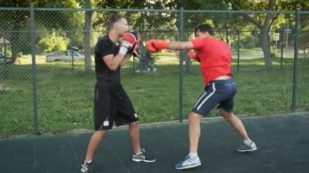 Boxeo. Un joven de apariencia caucásica entrena con su entrenador en la calle. Deportes y salud — Vídeos de Stock